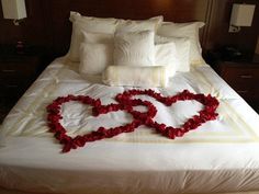 a bed with white sheets and red rose petals in the shape of two hearts on it