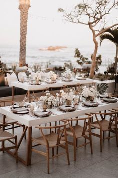 an outdoor dining table set up with white flowers and greenery on the tables, along with candles and place settings