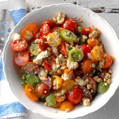 a white bowl filled with tomatoes, cucumbers and other vegetables next to a fork