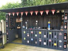 an outdoor bar with lots of beer bottles on the wall and flags hanging from it