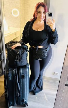 a woman taking a selfie in front of a mirror with her suitcase and cell phone