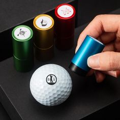 a person holding a golf ball next to three different colored balls on a black surface