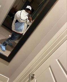 a man taking a selfie in the mirror with his cell phone while wearing blue jeans and a white jacket