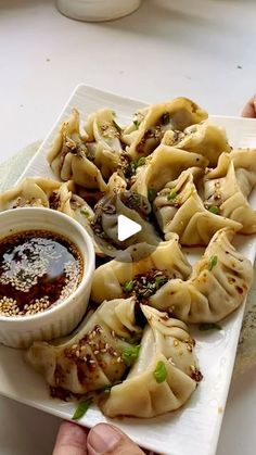 a person is holding a plate with dumplings and dipping sauce