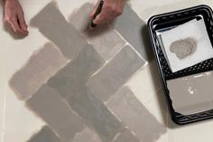 a person is using a brush to paint a brick pattern on the floor with gray and white colors