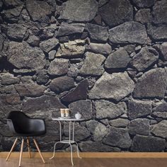 a chair and table in front of a stone wall with coffee mugs on it