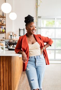 a woman standing in front of a counter wearing ripped jeans and a red cardigan