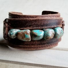 Distressed Finish Leather Cuff features a genuine strand of chunky African Turquoise. Each strand is different and will show varying shades of the natural stone. ***Please view all the pictures as they show examples of the many stone colors Cuff measures 2" by 9" in length Adjustable to 7" and 7.5" Although your item will resemble the photo, each piece is created by hand, so no two are identical.Thank you for visiting The Jewelry Junkie! Adjustable Turquoise Leather Bracelet In Rustic Style, Adjustable Rustic Turquoise Leather Bracelet, Southwestern Adjustable Cuff Bracelet With Natural Stones, Rustic Handmade Turquoise Cuff Bracelet, Adjustable Turquoise Cuff Bracelet With Natural Stones, African Turquoise, Wide Cuff, Leather Cuffs, Art Clothes