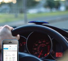 a car dashboard with a cell phone in the foreground and a hand on the steering wheel