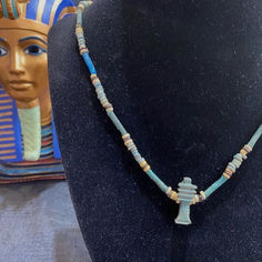 A 19 inch long ancient Egyptian necklace featuring tubular and disc shaped faience beads of blue and tan colors.  Hanging from the faience necklace is a blue faience Djed Pillar amulet that symbolizes stability and endurance and is associated with the backbone of Osiris.  Circa 700 to 30 BC. Djed Pillar, Tan Color