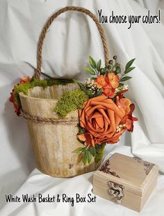 an orange flower arrangement in a basket next to a wooden box on a white sheet