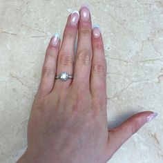 a woman's hand holding a diamond ring on her left hand, with light blue and white nail polish