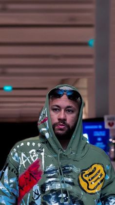 a man wearing a green hoodie with graffiti on it's chest and sunglasses