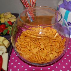 a bowl filled with cereal next to apples and strawberries on a pink table cloth