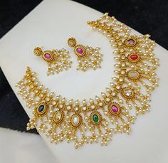 luxurious Antique look Navratna necklace set, featuring a dazzling array of multicolored gemstones encircled by radiant pearl accents. This exquisite set includes a stunning necklace and matching earrings, each piece meticulously crafted with intricate gold-tone details. Ideal for weddings, festivities, or as a treasured gift, this set embodies elegance and sophistication. Elevate your ensemble with this captivating jewelry set, designed to add a touch of glamour and richness to any occasion. Navratna Necklace, Indian Wedding Jewelry Sets, American Diamond Necklaces, Necklace Matching, Temple Jewelry, Bridal Jewelry Collection, Indian Wedding Jewelry, Bridal Jewellery Indian, Temple Jewellery