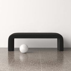 a white ball sitting on top of a black bench in front of a white wall