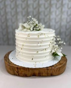 a white wedding cake with flowers on top sitting on a wooden board in front of a wall