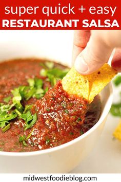 a hand dipping a tortilla chip into a bowl of salsa