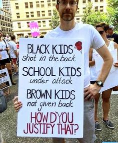 a man holding a sign that says black kids shot in the back school kids under attack brown kids not given back