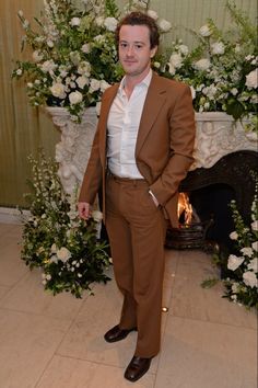 a man in a brown suit standing next to a floral display with white and green flowers