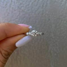 a woman's hand holding an engagement ring with three diamonds on it, in front of a white wall