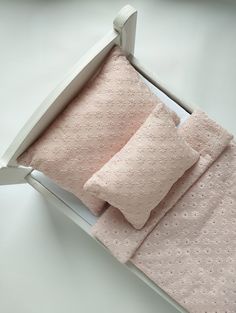 a bed with pink sheets and pillows in a white wooden frame on top of a table