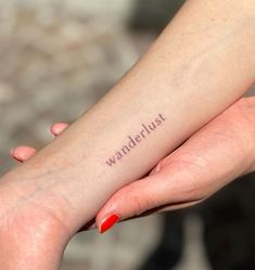 a woman's arm with the word wanderlust tattooed on it, in red ink