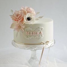 a white cake with pink flowers on top sitting on a glass stand in front of a white background