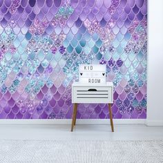 a room with purple and blue mermaid scales on the wall next to a white dresser