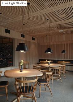 an empty restaurant with wooden tables and black lamps hanging from the ceiling, along with chairs