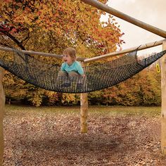 a little boy sitting in a hammock with leaves on the ground around him