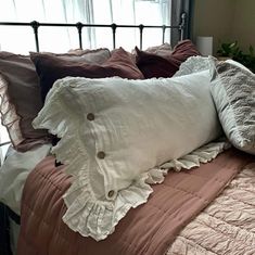 a bed topped with lots of pillows next to a metal headboard and window sill