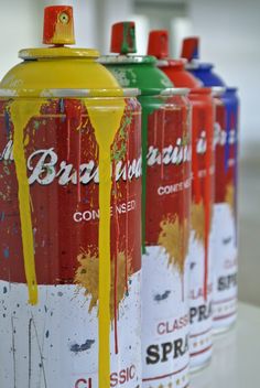 four cans of soda with yellow, red, and green paint splattered on them