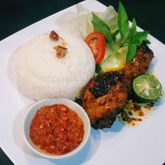 a white plate topped with meat and rice next to a small bowl of sauce on the side