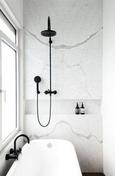 a white bath tub sitting under a window next to a wall mounted faucet