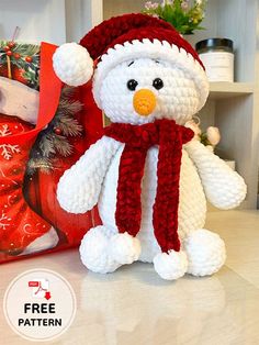 a crocheted snowman stuffed animal sitting next to a christmas present bag with the word free pattern on it