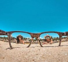 two people wearing hats and sunglasses on the beach with palm trees reflected in their glasses