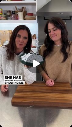 two women standing in a kitchen, one holding a bowl of food and the other holding a plate with marshmallows on it