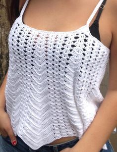 a woman standing next to a tree with her hand on her hip wearing a white crocheted tank top