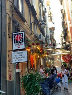 people are walking down the street in front of shops with signs and plants on them