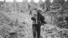 a man carrying a child walks through rubble