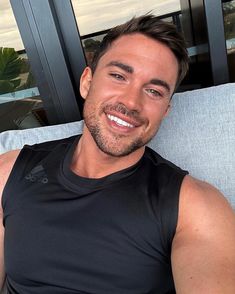 a man sitting on top of a blue couch next to a window smiling at the camera