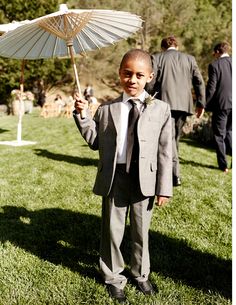 a young boy in a suit and tie holding an umbrella