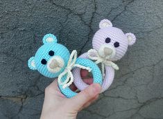 two crocheted teddy bears are being held by someone's hand on the ground