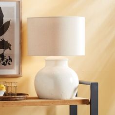 a white vase sitting on top of a wooden table next to a framed painting and a lamp