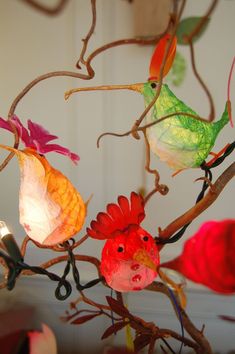 three colorful birds sitting on top of a branch next to a light fixture with leaves