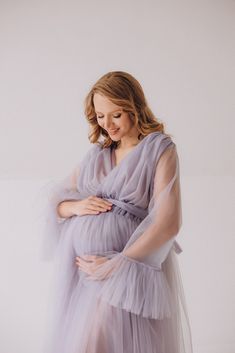 a pregnant woman wearing a purple dress and holding her belly in front of the camera