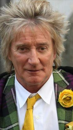 an older man with blonde hair wearing a yellow tie and plaid jacket, looking at the camera