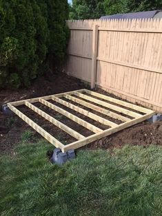 a wooden bed frame sitting in the middle of a yard next to a fence and grass