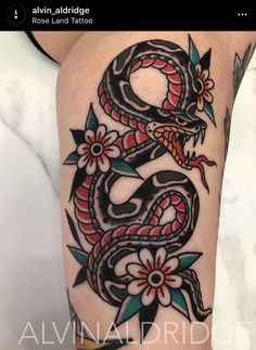 a black and red dragon tattoo on the thigh, with flowers in front of it